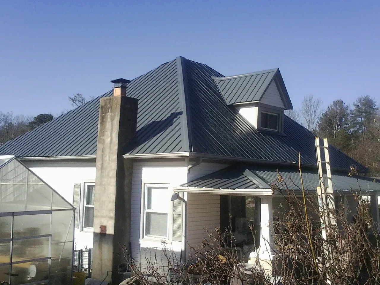 Dark blue standing seam metal roof on a white farmhouse with dormer — Slate & Tile Roof Repair by Roofing Brothers in Mentcle