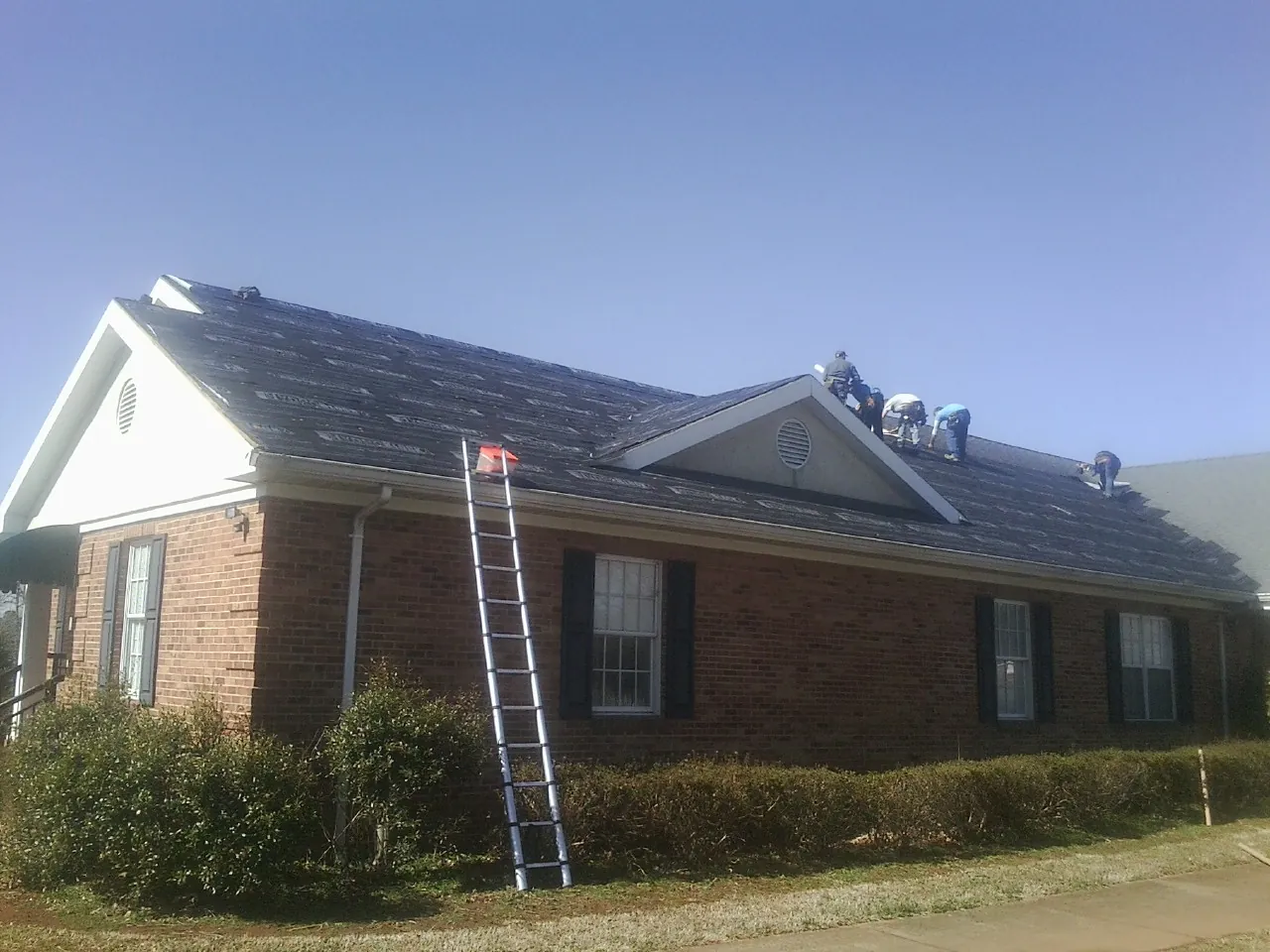 Crew tearing shingles off a brick ranch roof with a ladder set — Metal Roof Repair work by our crew in Mentcle