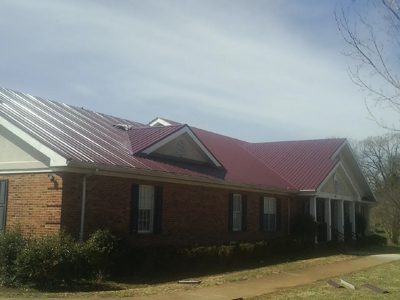 Red metal roof with gabled entries on a long brick building, from a Hail Damage Roof Repair job in Mentcle