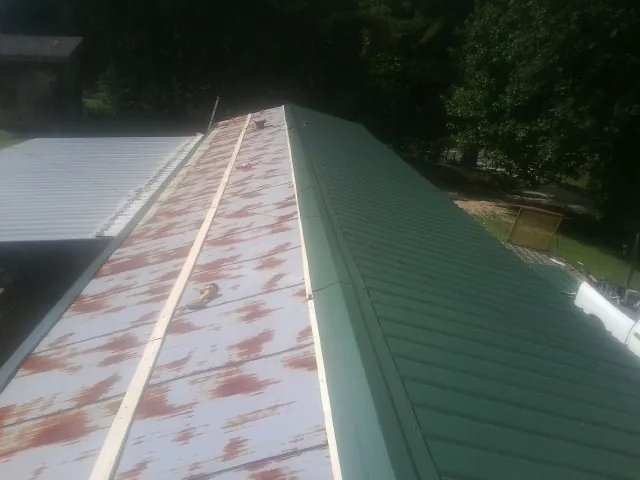 Old rusted panels beside newly installed green metal roofing — Wind Damage Roof Repair by Roofing Brothers in Mentcle