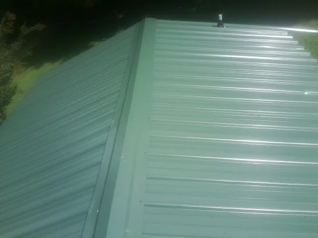 New green metal panels meeting at the ridge of a roof — Flat Roof Repair work by our crew in Mentcle