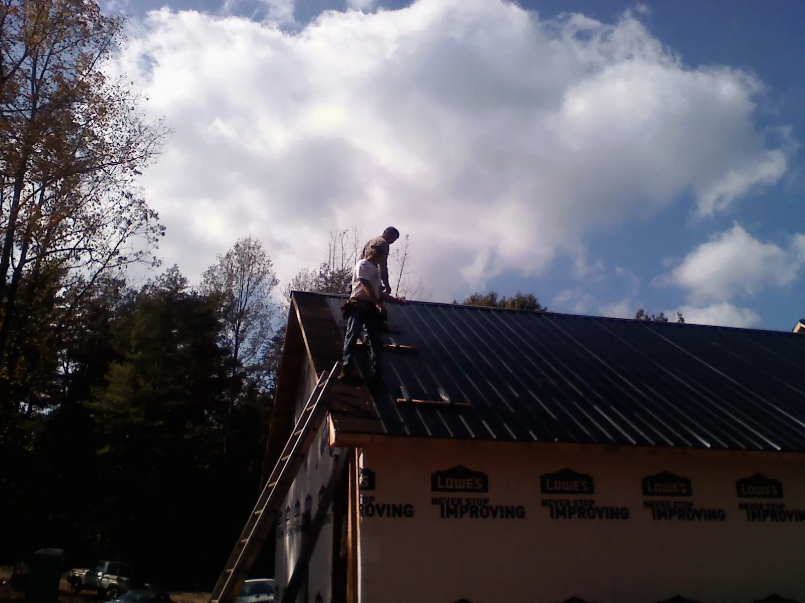 Roofer fastening dark metal panels high against a cloudy sky, from a Roof Inspection job in Mentcle