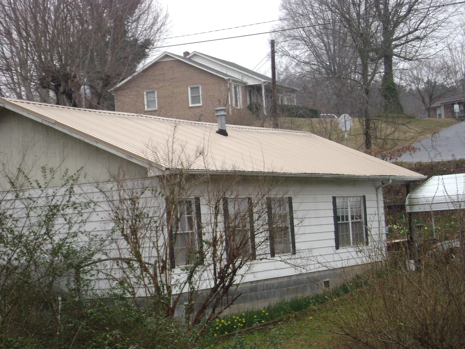 Tan metal roof on a white sided house set into a hillside — Commercial Roofing by Roofing Brothers in Mentcle